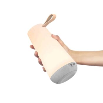 A hand holding the Uma Mini, a beige cylindrical smart speaker with a strap, featuring a speaker grille at the bottom.