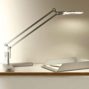 A lit Link Clamp lamp with an adjustable arm is positioned on a cabinet next to a paper tray containing a pen.