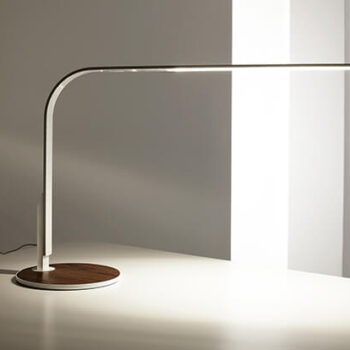 The LIM 360, a sleek modern desk lamp featuring a curved arm and thin horizontal light strip, is placed on a white table.