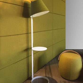 The Lana Floor, a modern green floor lamp with a round base and small shelf, stands against a green paneled wall. A matching green ottoman sits nearby on the wooden floor.