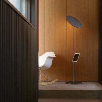 The modern room features a white rocking chair, the Circa Floor supporting a tablet, and wooden paneling in the background.