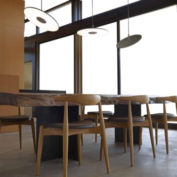 The Circa Floor lamp illuminates a modern dining area with wooden chairs arranged around a long table, complemented by pendant lights over large windows.