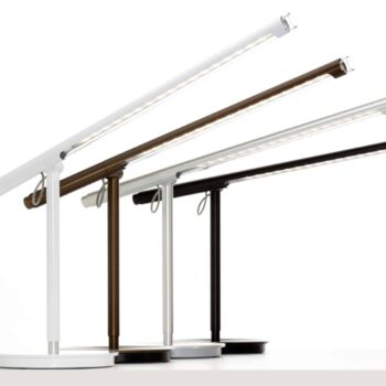 Four Brazo Floor adjustable desk lamps in black, white, and brown are arranged in a row on a white surface.