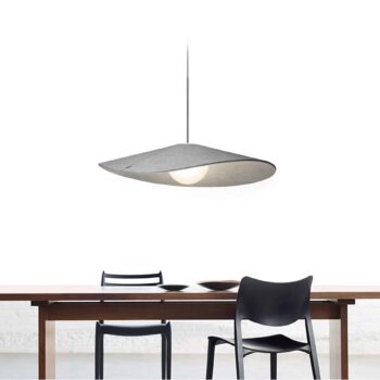 The Bola Felt pendant lamp with a sleek gray shade hangs above a minimalist wooden table and two black chairs against a white background.