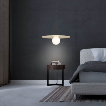 Modern bedroom featuring a Bola Disc hanging lamp, small round bedside table with books, and a gray upholstered bed against a dark wall.