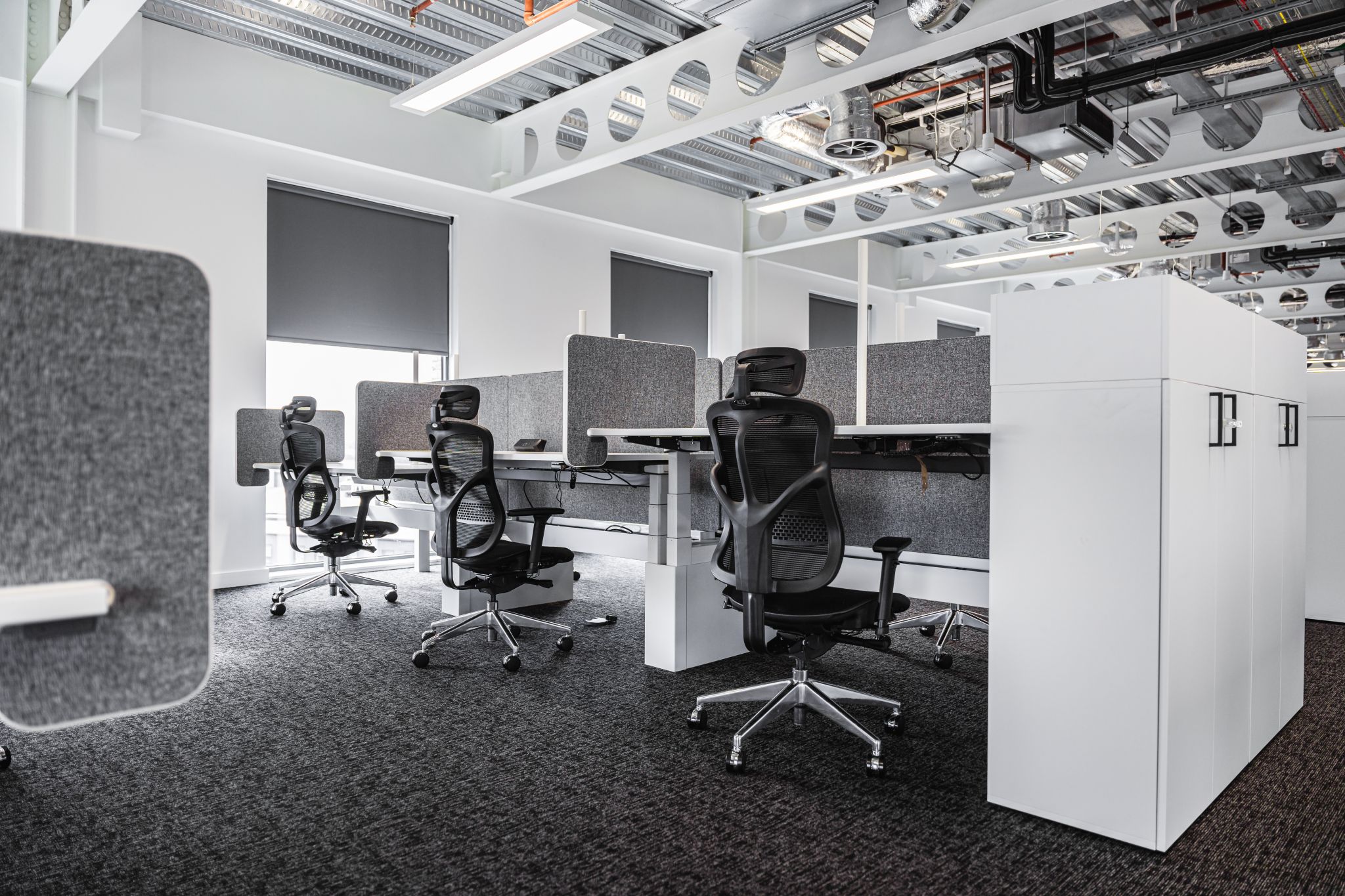 Modern office space featuring several empty workstations, gray partitions, exposed ceiling pipes, and ergonomic F94 Chairs.