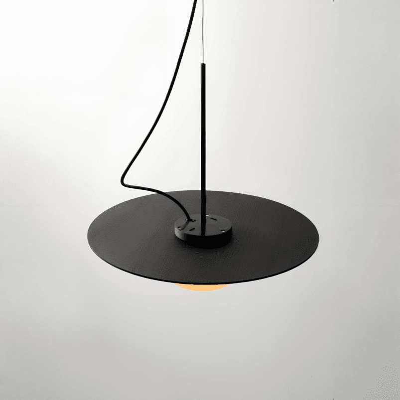 A modern, minimalist black pendant light with a flat circular shade hangs from the ceiling, creating ambience against a plain white background—perfect lighting for autumn evenings.