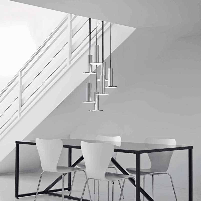 Minimalist dining area with a black table, four white chairs, and modern pendant lights under a white staircase in a bright room, enhanced by autumn lighting that adds warmth and ambience.