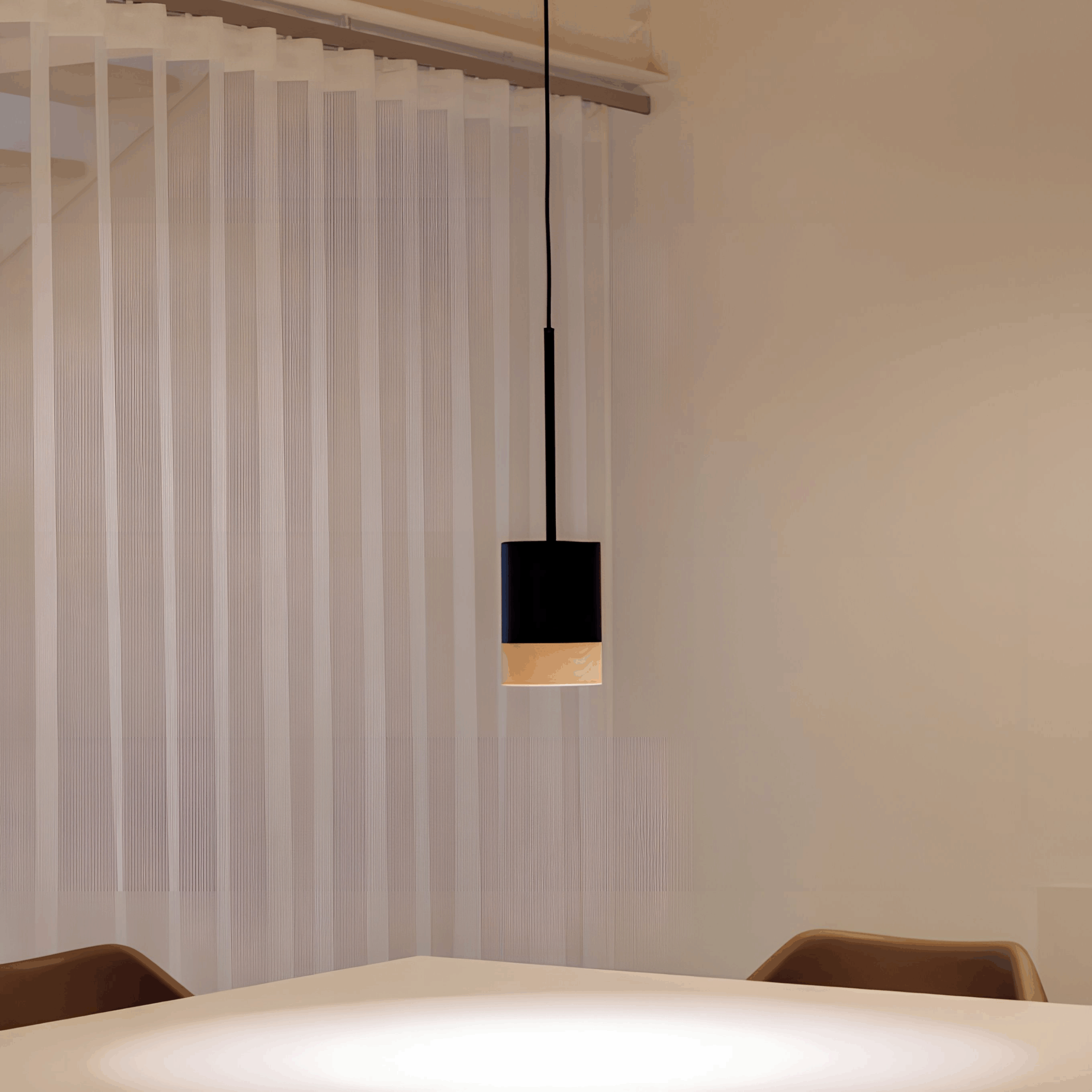A black pendant light brings warmth and ambience above a white table with two brown chairs, set against a background of sheer vertical blinds.