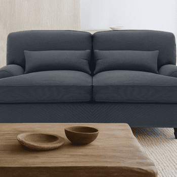 The Oxford Sofa, in dark grey upholstery with two matching cushions, sits behind a wooden coffee table holding two shallow wooden bowls in a neutral-toned living room.