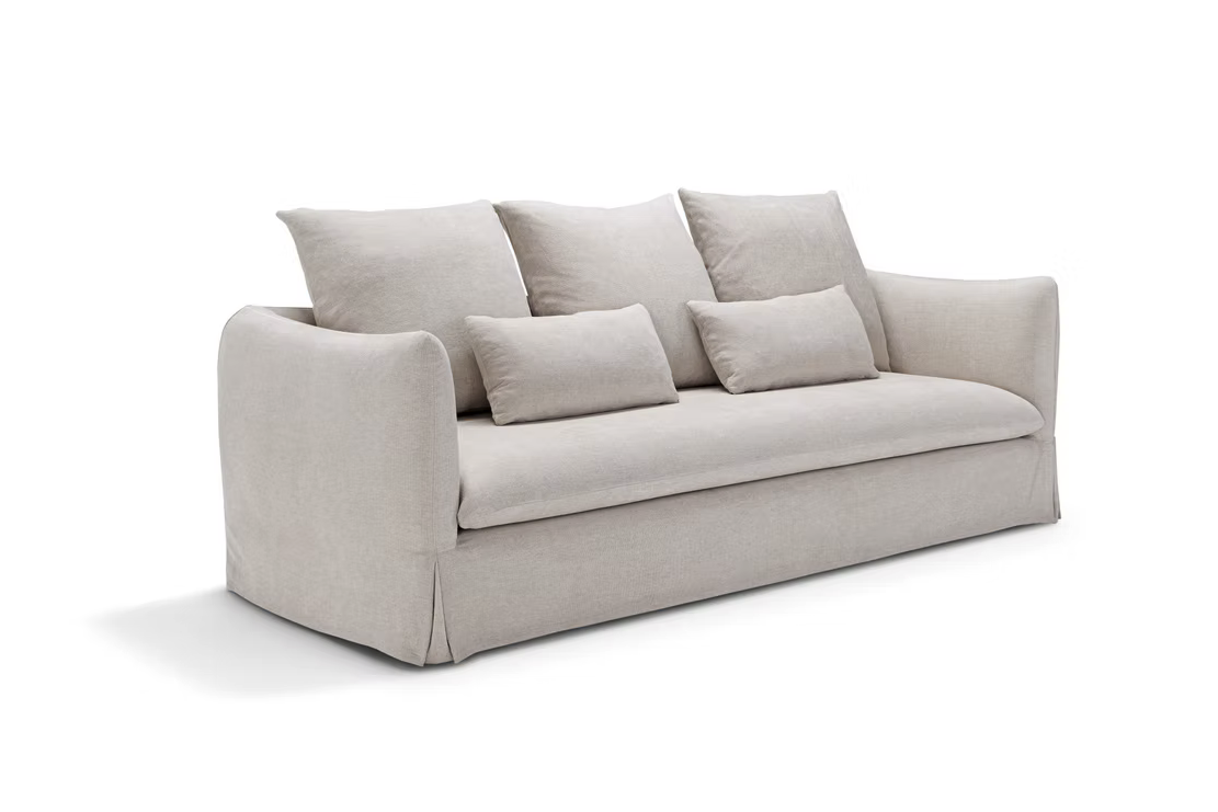The Dylan Sofa features light beige fabric upholstery, three large back cushions, and two smaller rectangular pillows, displayed against a plain white background.