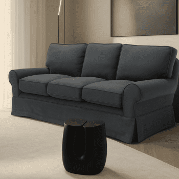 A Pantelleria Sofa with plush dark gray cushions sits in a modern living room beside a small black sculptural side table.