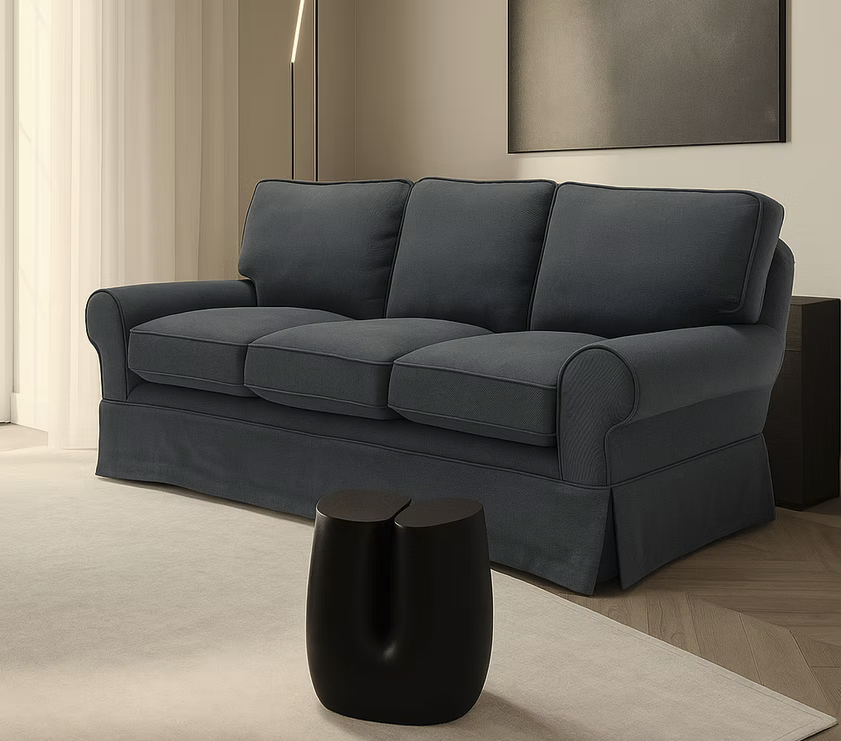 A Pantelleria Sofa with plush dark gray cushions sits in a modern living room beside a small black sculptural side table.