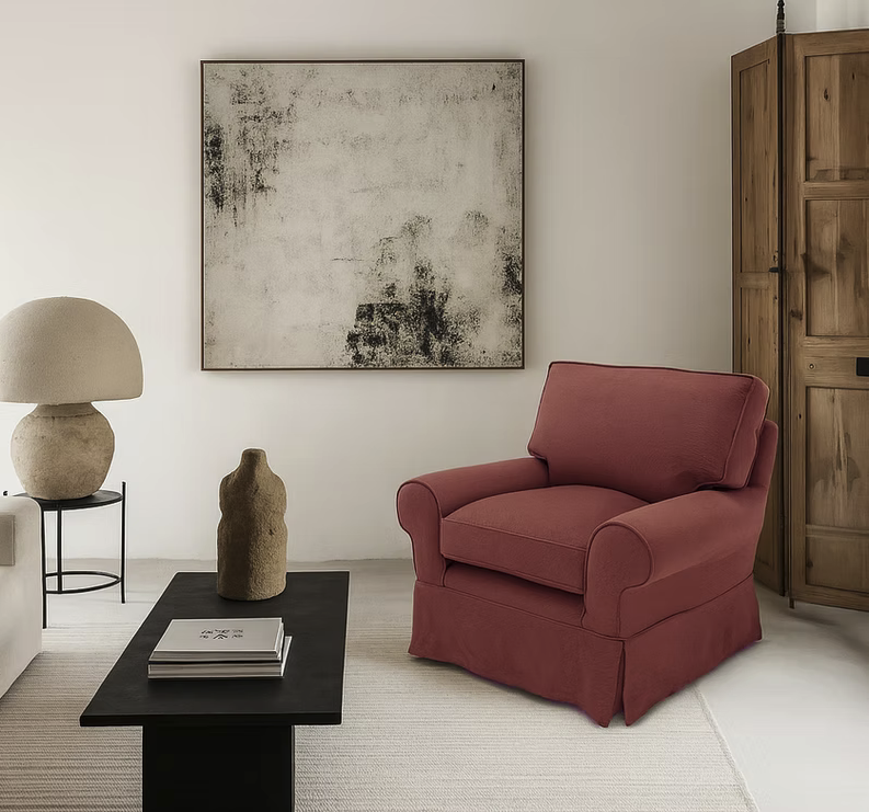 A living room featuring the Pantelleria Sofa, a large red armchair, black coffee table, abstract wall art, beige lamp, vase, and wooden cabinet.
