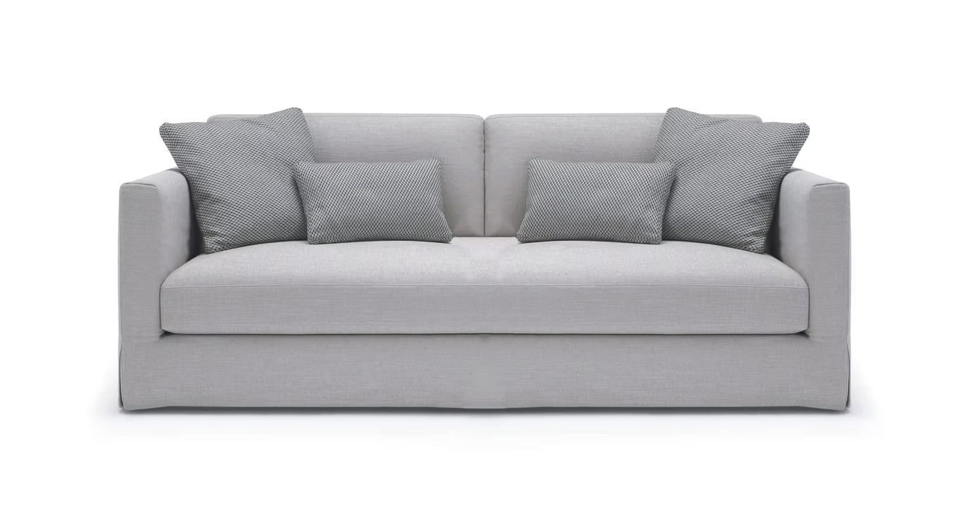 The John John Sofa is an large 2 seater with cushions and a left-side chaise, upholstered in light beige fabric, shown on a white background.