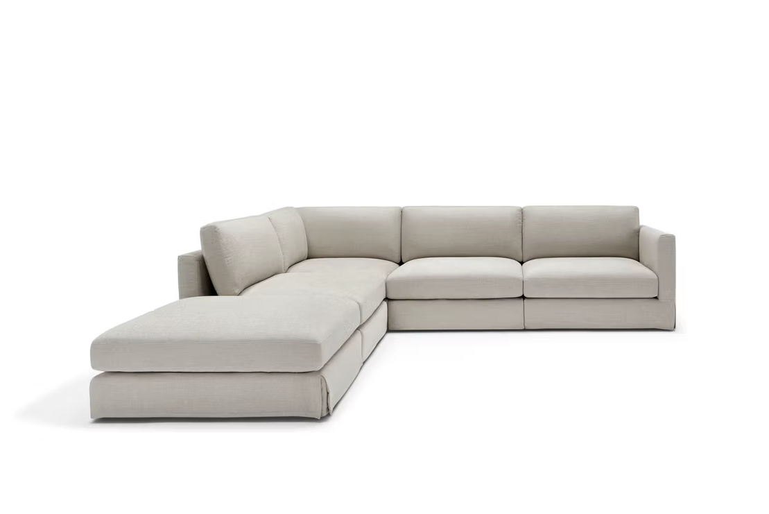The John John Sofa is an L-shaped sectional with three seat cushions and a left-side chaise, upholstered in light beige fabric, shown on a white background.