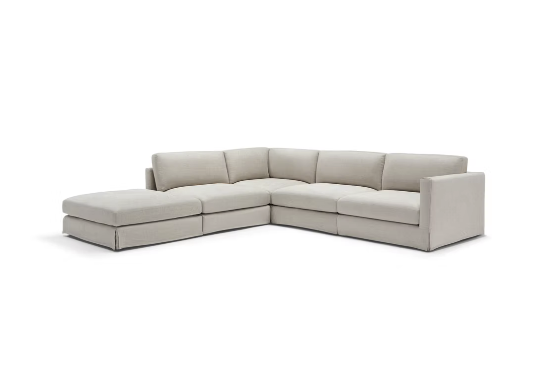 The John John Sofa is an L-shaped sectional with wide seat cushions, a left-side chaise, right armrest, and light beige upholstery, displayed against a plain white background.