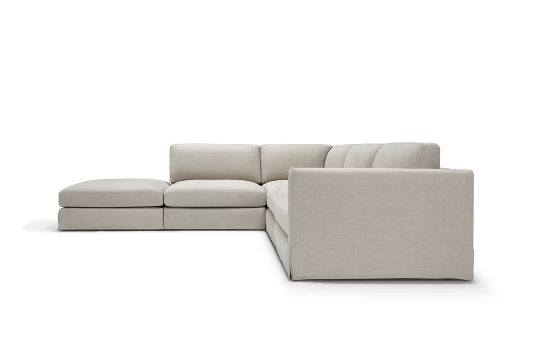 The John John Sofa is an L-shaped sectional in light beige with three seat and back cushions plus a left-side chaise lounge, shown against a white background.