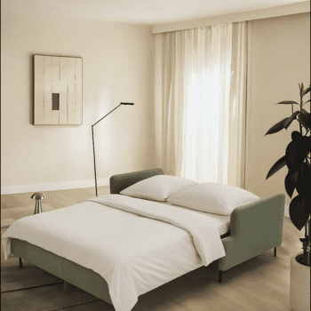 Minimalist bedroom with a green Tower Sofa-bed, white bedding, floor lamp, abstract wall art, sheer curtains, plant, and neutral-toned walls and flooring.