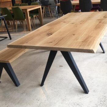 A LOOP Delta table with a matching bench, both featuring light wood surfaces and black LOOP metal legs, displayed in a showroom among other tables and chairs.