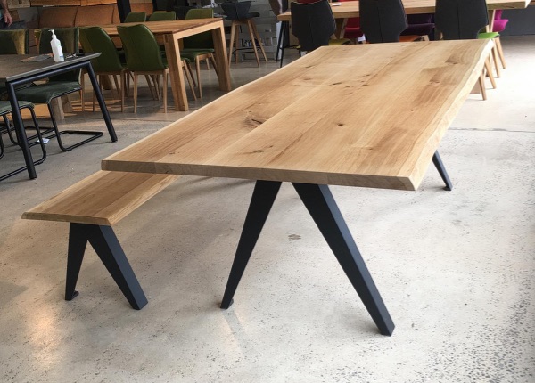 A LOOP Delta table with a matching bench, both featuring light wood surfaces and black LOOP metal legs, displayed in a showroom among other tables and chairs.