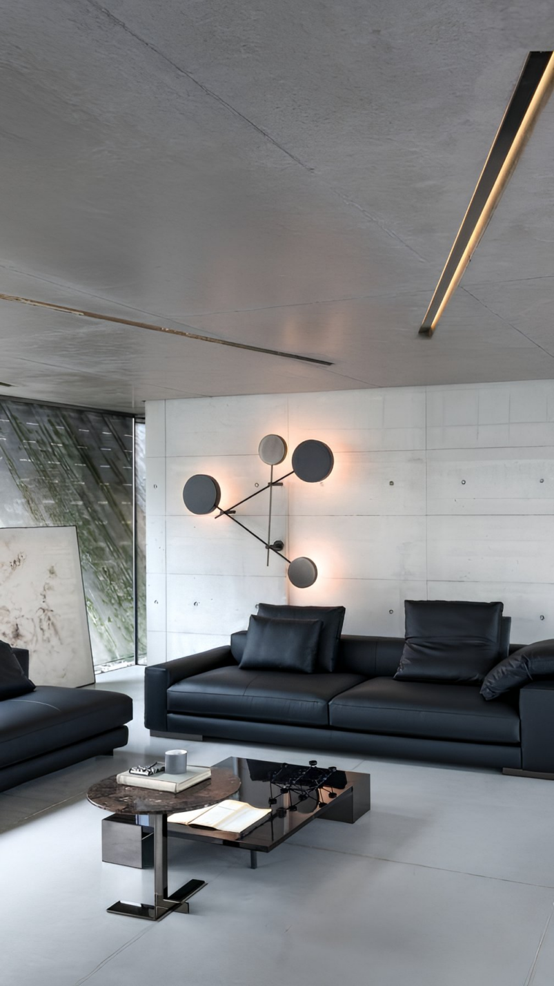 Modern living room with black leather sofas, a geometric wall lamp, a round coffee table with books and decor, and concrete ceiling and walls—perfect inspiration for bedroom decorating or how to furnish a bedroom with contemporary style.